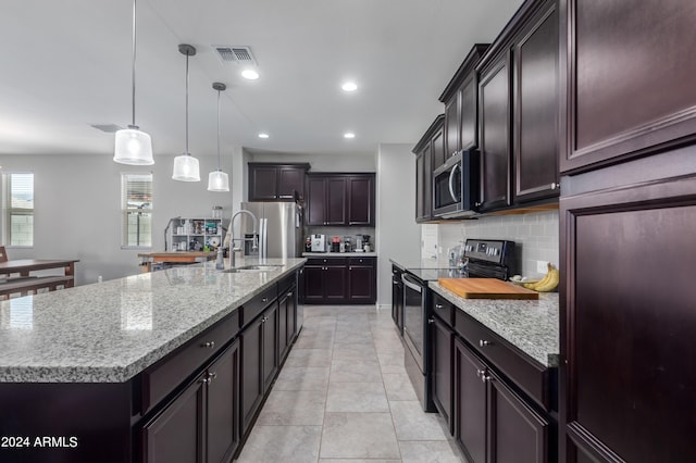 kitchen with pendant lighting, appliances with stainless steel finishes, light tile floors, a center island with sink, and tasteful backsplash