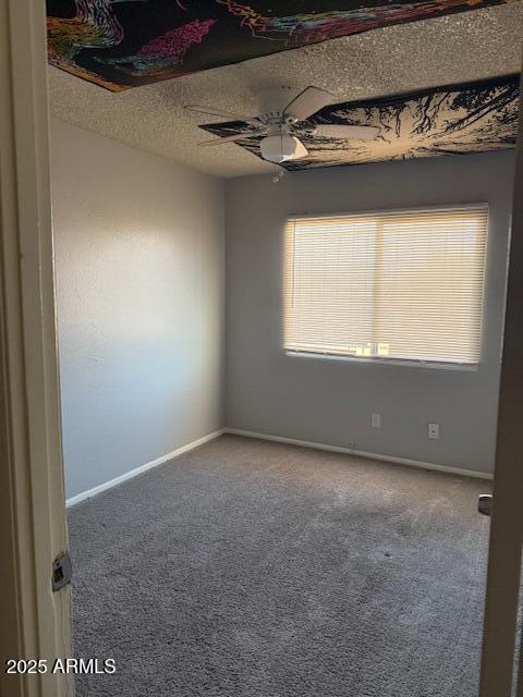 carpeted empty room featuring a textured ceiling, ceiling fan, and baseboards