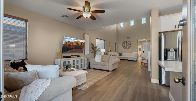 living area featuring ceiling fan, a high ceiling, wood finished floors, visible vents, and baseboards