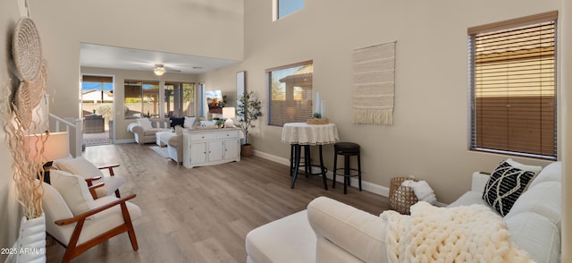 living room featuring a ceiling fan, a high ceiling, baseboards, and wood finished floors