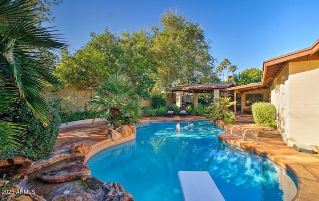 pool with a patio area, fence, and a diving board