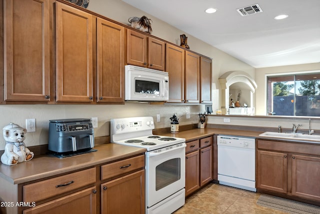 kitchen with a sink, visible vents, white appliances, and brown cabinets