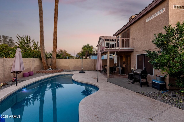 pool at dusk with area for grilling and a patio area