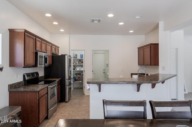 kitchen featuring kitchen peninsula, appliances with stainless steel finishes, sink, light tile patterned floors, and a breakfast bar area