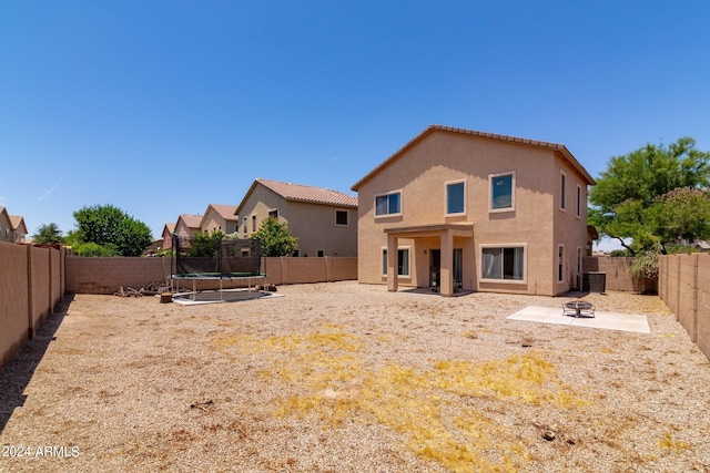 back of property with a fire pit, a trampoline, and central air condition unit