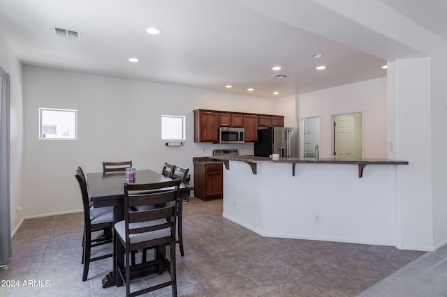 kitchen featuring sink, kitchen peninsula, a kitchen bar, light tile patterned floors, and appliances with stainless steel finishes