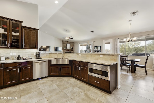 kitchen featuring dark brown cabinetry, decorative light fixtures, stainless steel appliances, a sink, and glass insert cabinets