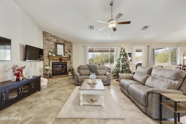 living room featuring lofted ceiling, ceiling fan, visible vents, and a stone fireplace