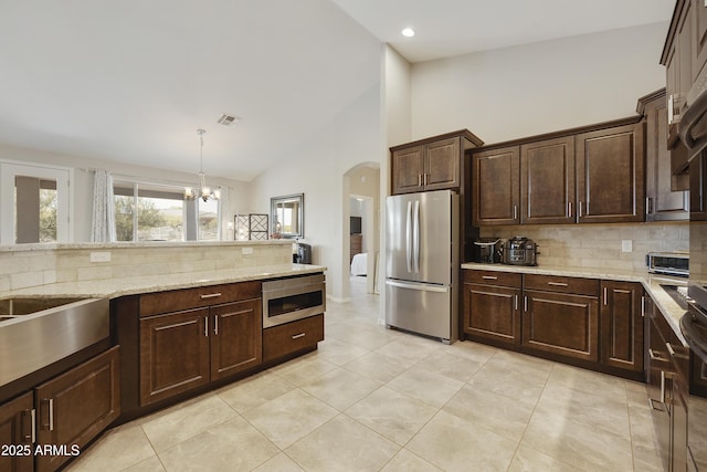 kitchen featuring dark brown cabinetry, visible vents, appliances with stainless steel finishes, decorative light fixtures, and light stone countertops