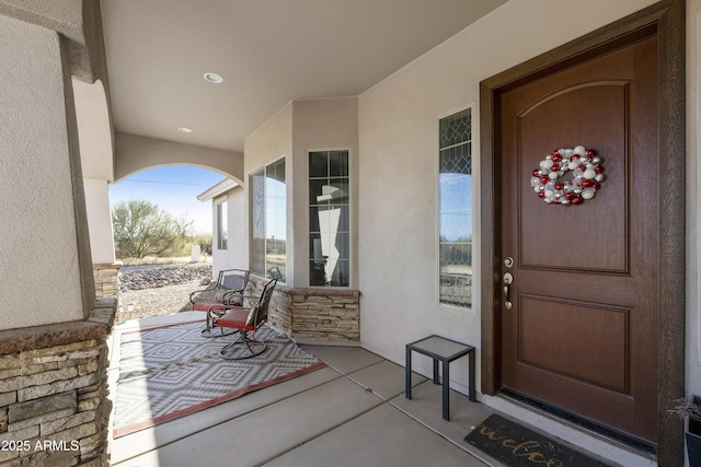 entrance to property featuring stone siding, a porch, and stucco siding