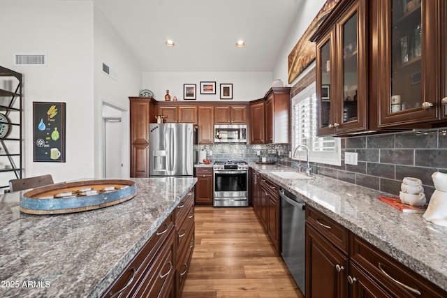 4029 N 160th Dr, Goodyear, AZ 85395 - kitchen featuring stainless steel appliances, light stone counters, light wood-style floors, decorative backsplash, and glass insert cabinets