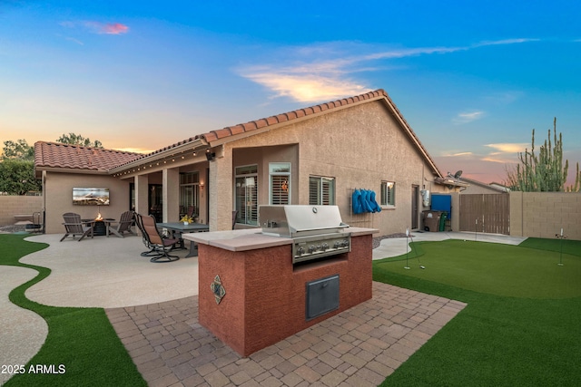 4029 N 160th Dr, Goodyear, AZ 85395 - back of house at dusk with an area to practice putting, a patio, a fenced backyard, and an outdoor kitchen
