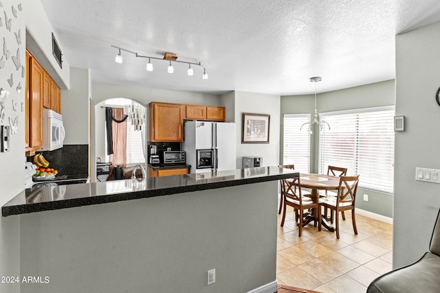 kitchen with white appliances, light tile patterned floors, a textured ceiling, decorative light fixtures, and kitchen peninsula