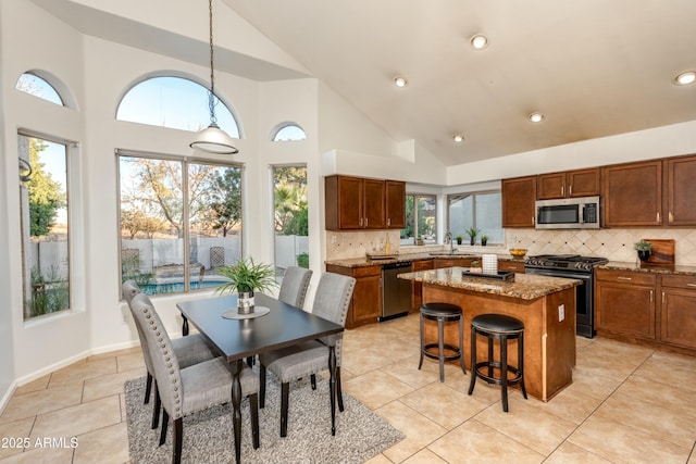 kitchen featuring appliances with stainless steel finishes, a kitchen island, stone countertops, backsplash, and hanging light fixtures