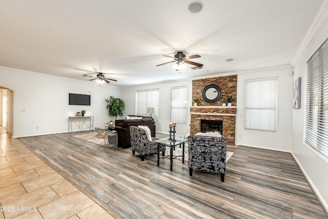 living room featuring ceiling fan, wood-type flooring, a large fireplace, and crown molding