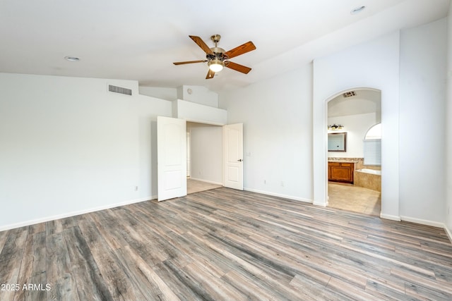 interior space with ceiling fan, connected bathroom, hardwood / wood-style flooring, and vaulted ceiling