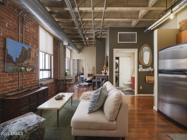 114 W Adams St Unit 907, Phoenix, AZ 85003 - living area featuring stacked washer / dryer, brick wall, wood-type flooring, a high ceiling, and baseboards