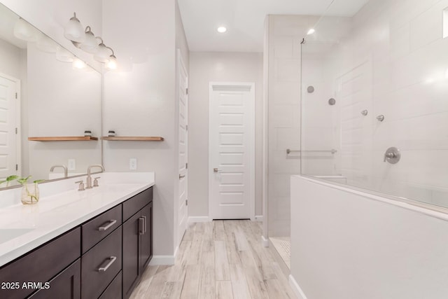 full bath with wood finished floors, a sink, walk in shower, double vanity, and baseboards