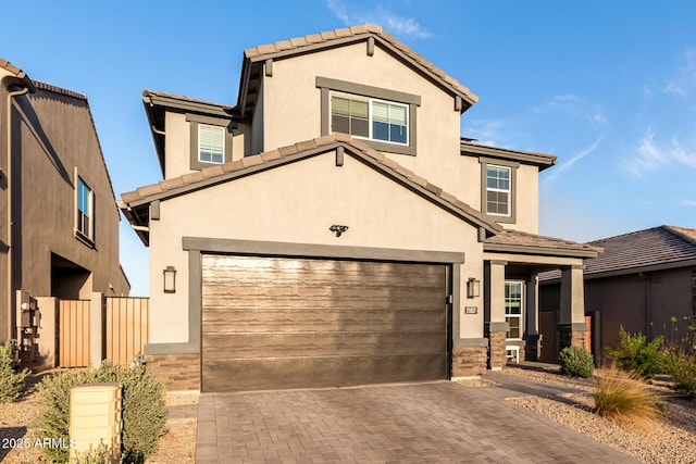 view of front facade featuring a garage, stucco siding, a tiled roof, and decorative driveway