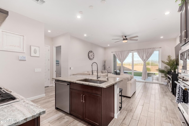 kitchen featuring an island with sink, light wood-style flooring, a ceiling fan, appliances with stainless steel finishes, and a sink
