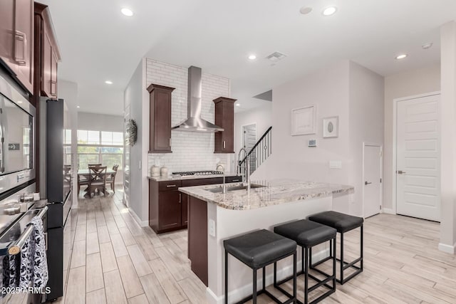 kitchen featuring stainless steel appliances, light wood-style flooring, wall chimney exhaust hood, and decorative backsplash