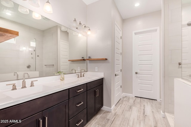 full bath featuring a tile shower, wood finished floors, double vanity, and a sink