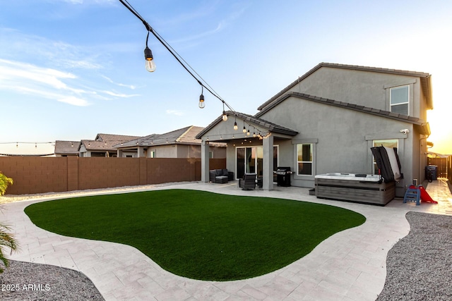 rear view of property featuring a patio, stucco siding, a fenced backyard, a hot tub, and a lawn