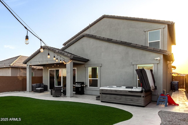 rear view of house featuring a hot tub, a yard, fence, a patio, and stucco siding