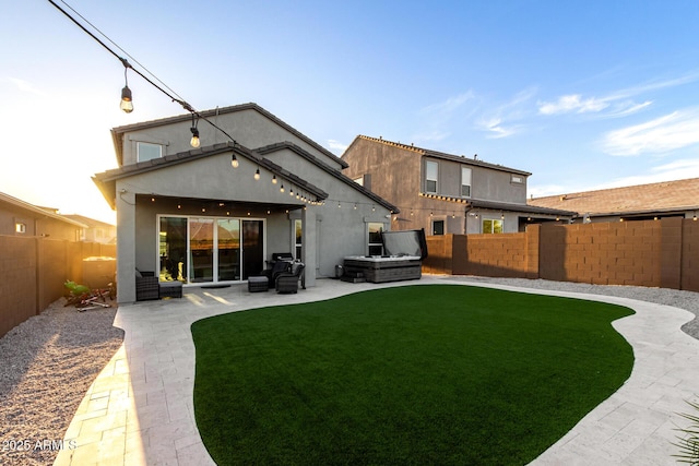 rear view of property with stucco siding, a patio area, a fenced backyard, a hot tub, and a yard