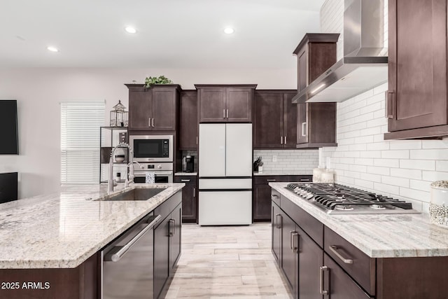 kitchen featuring a sink, wall chimney range hood, appliances with stainless steel finishes, dark brown cabinetry, and decorative backsplash