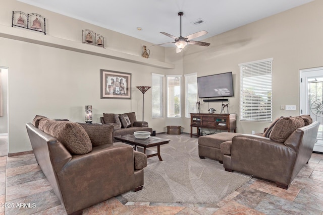 living area featuring a ceiling fan, stone finish floor, a healthy amount of sunlight, and visible vents