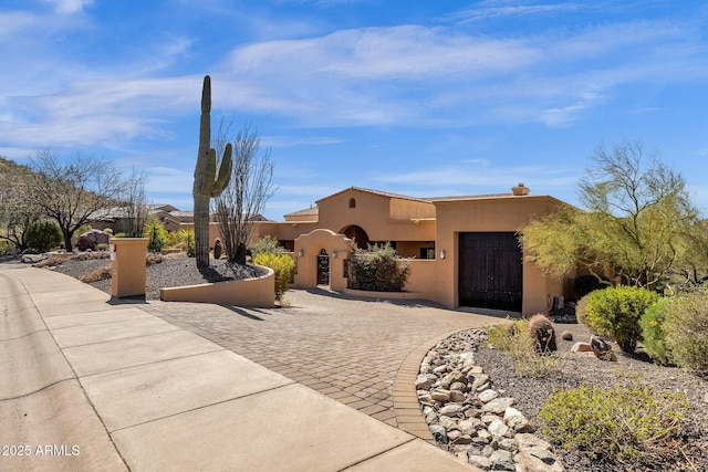 pueblo-style house with a garage, decorative driveway, and stucco siding