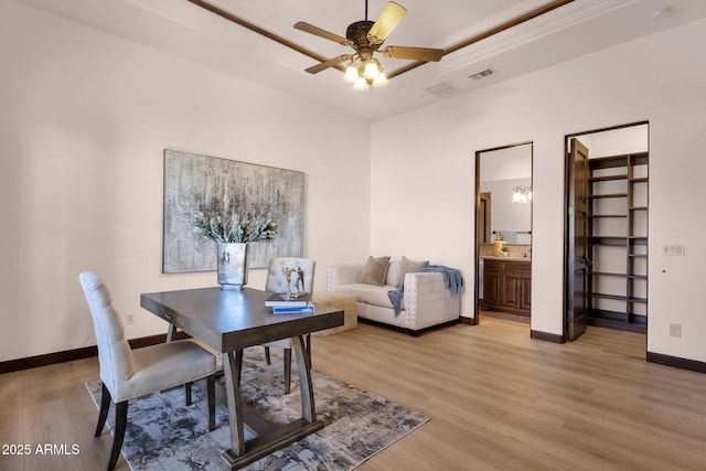 home office featuring a ceiling fan, a raised ceiling, light wood-style flooring, and baseboards