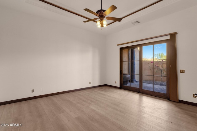 empty room featuring light wood-style flooring, a ceiling fan, visible vents, baseboards, and a tray ceiling