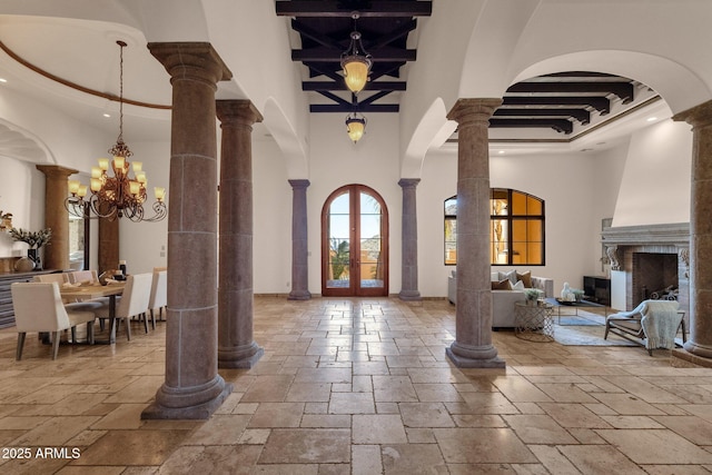 entryway featuring ornate columns, a notable chandelier, stone tile flooring, and french doors