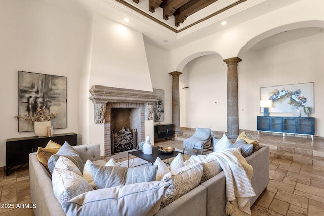 living area with arched walkways, stone tile floors, a towering ceiling, ornamental molding, and ornate columns