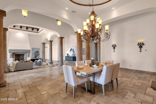 dining room with decorative columns, arched walkways, a raised ceiling, and stone tile flooring