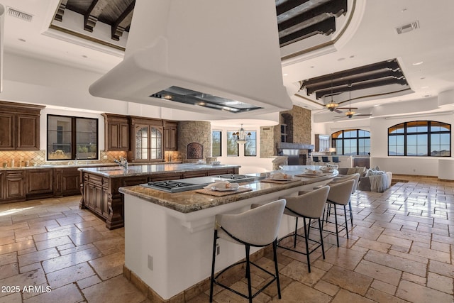 kitchen featuring an island with sink, stone tile floors, a tray ceiling, and ventilation hood