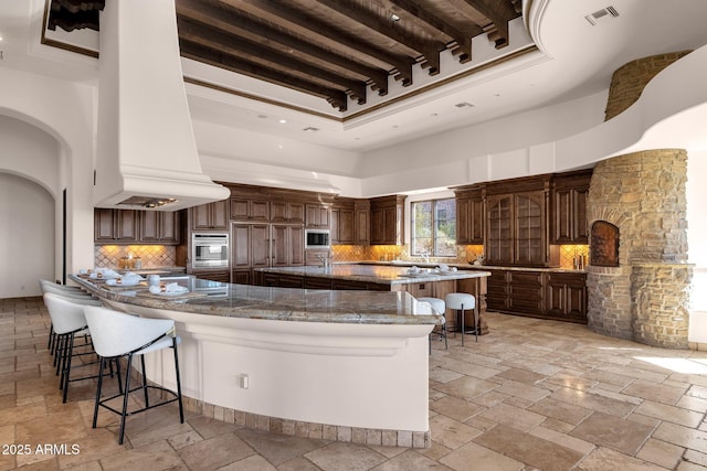 kitchen with stone tile floors, a breakfast bar, a spacious island, stainless steel oven, and visible vents