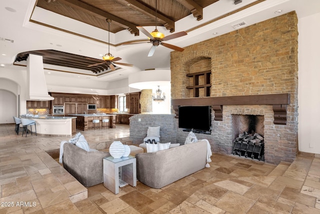 living room featuring stone tile floors, visible vents, wood ceiling, ceiling fan, and a tray ceiling