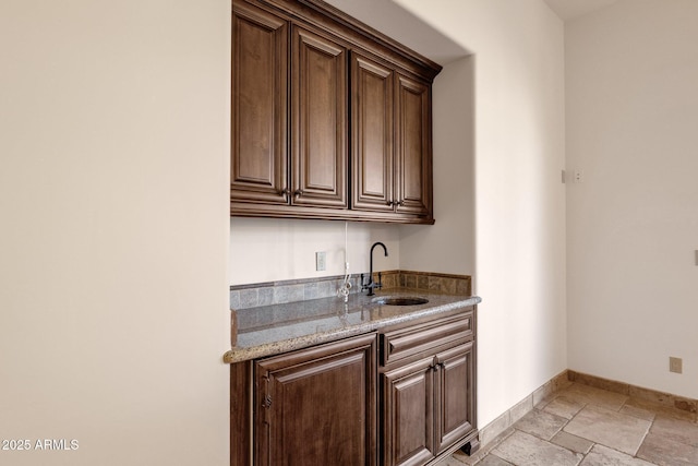 bar featuring baseboards, a sink, and stone tile floors