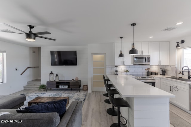 kitchen featuring sink, appliances with stainless steel finishes, hanging light fixtures, white cabinets, and light wood-type flooring