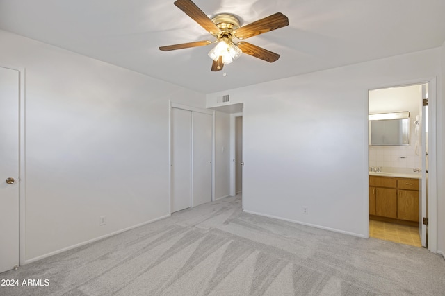 unfurnished bedroom with light colored carpet, connected bathroom, sink, and ceiling fan