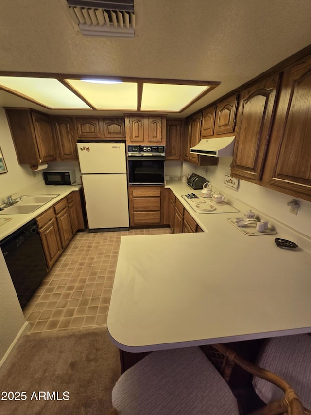 kitchen with black appliances, a sink, under cabinet range hood, a peninsula, and light countertops