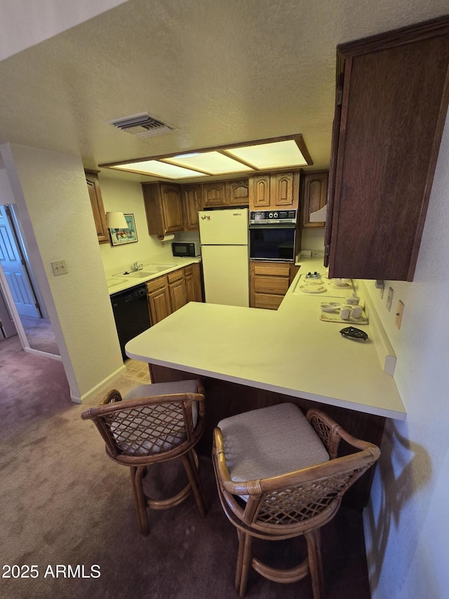 kitchen featuring visible vents, carpet, a kitchen breakfast bar, a peninsula, and black appliances