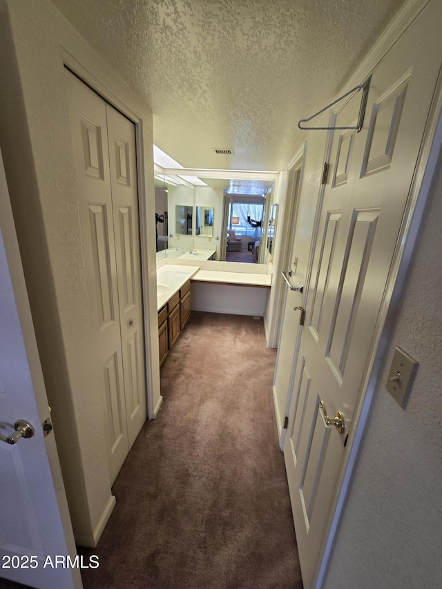 bathroom featuring visible vents, a textured ceiling, carpet, vanity, and a textured wall