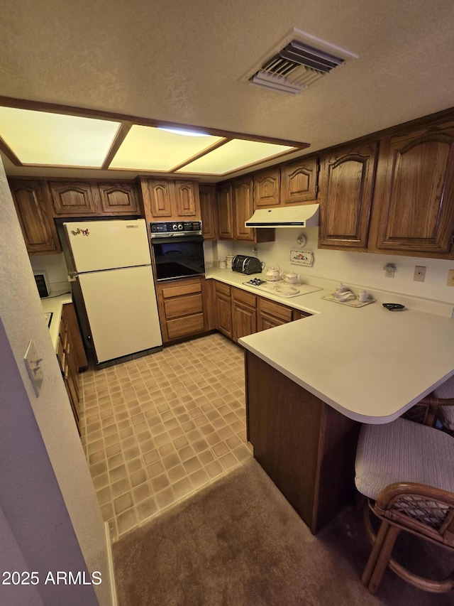 kitchen featuring visible vents, ventilation hood, a breakfast bar area, a peninsula, and white appliances