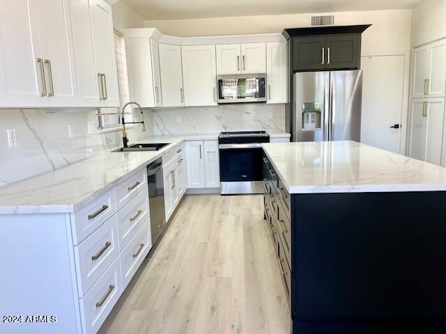 kitchen with white cabinetry, a kitchen island, stainless steel appliances, and light wood-type flooring