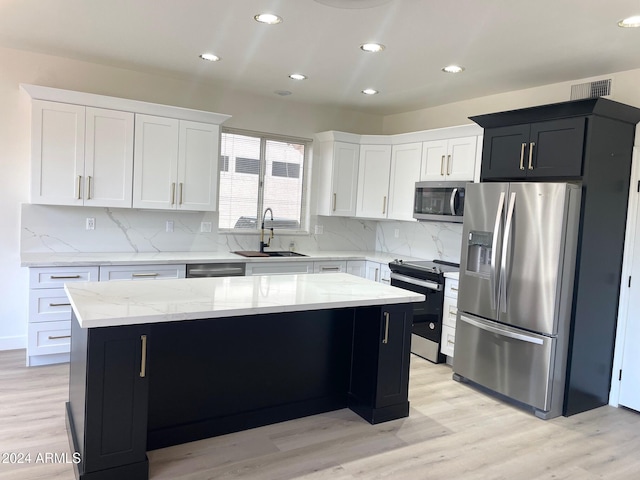 kitchen featuring sink, decorative backsplash, light wood-type flooring, appliances with stainless steel finishes, and a kitchen island