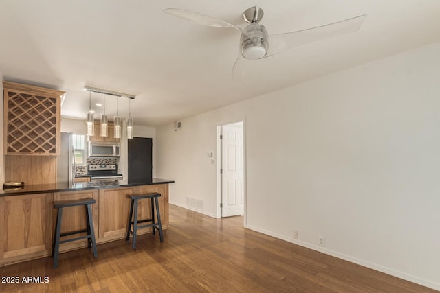 kitchen featuring appliances with stainless steel finishes, dark hardwood / wood-style flooring, a kitchen bar, hanging light fixtures, and kitchen peninsula